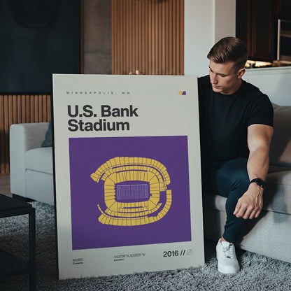 Man holding a large poster of U.S. Bank Stadium in a living room.