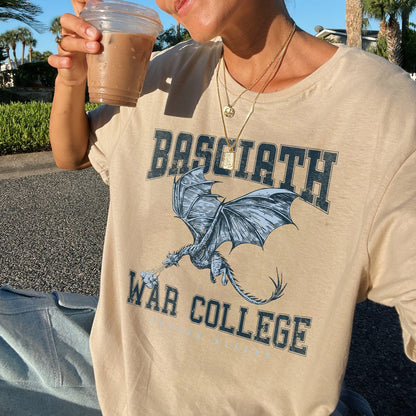 Person wearing a beige t-shirt with a dragon graphic and text, holding a cup outdoors.